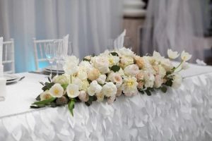 White flowers are arranged at the head of a wedding table