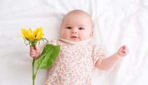 A baby holds a picked flower in her hands while laying down