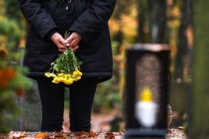 A woman holds yellow flowers in front of a grave