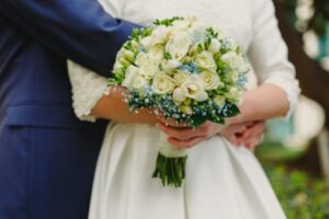 A bride holds a bouquet as her groom puts his arm around her